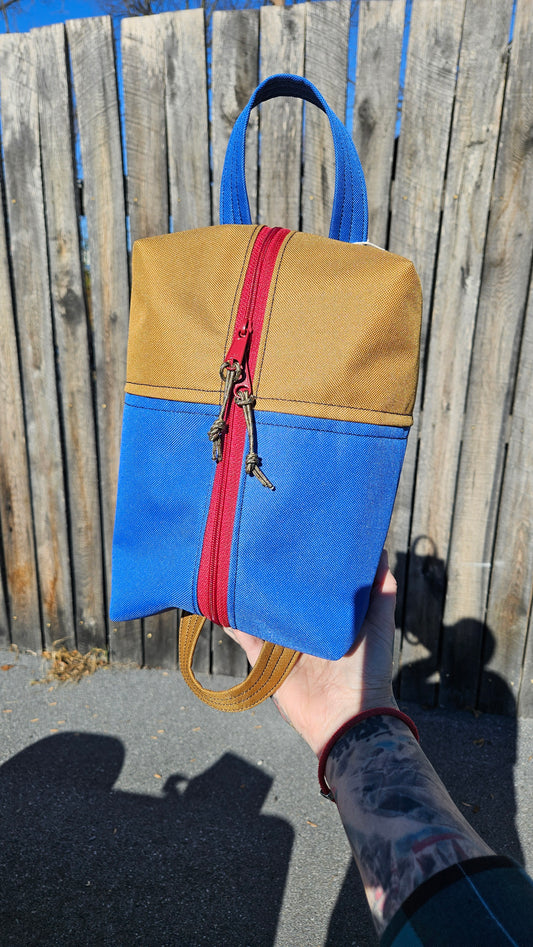 This Brown and Blue polycoated canvas zipper bag with a maroon zipper has two long handles on either end so you can hang it, or loop it around your handlebars!