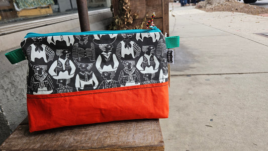 This fantastic bag is made of bright orange canvas on the botton and has patterned fabric on top with a zipper! Two tabs on each end and a paracord pull make it easy to open and close this rad bag.